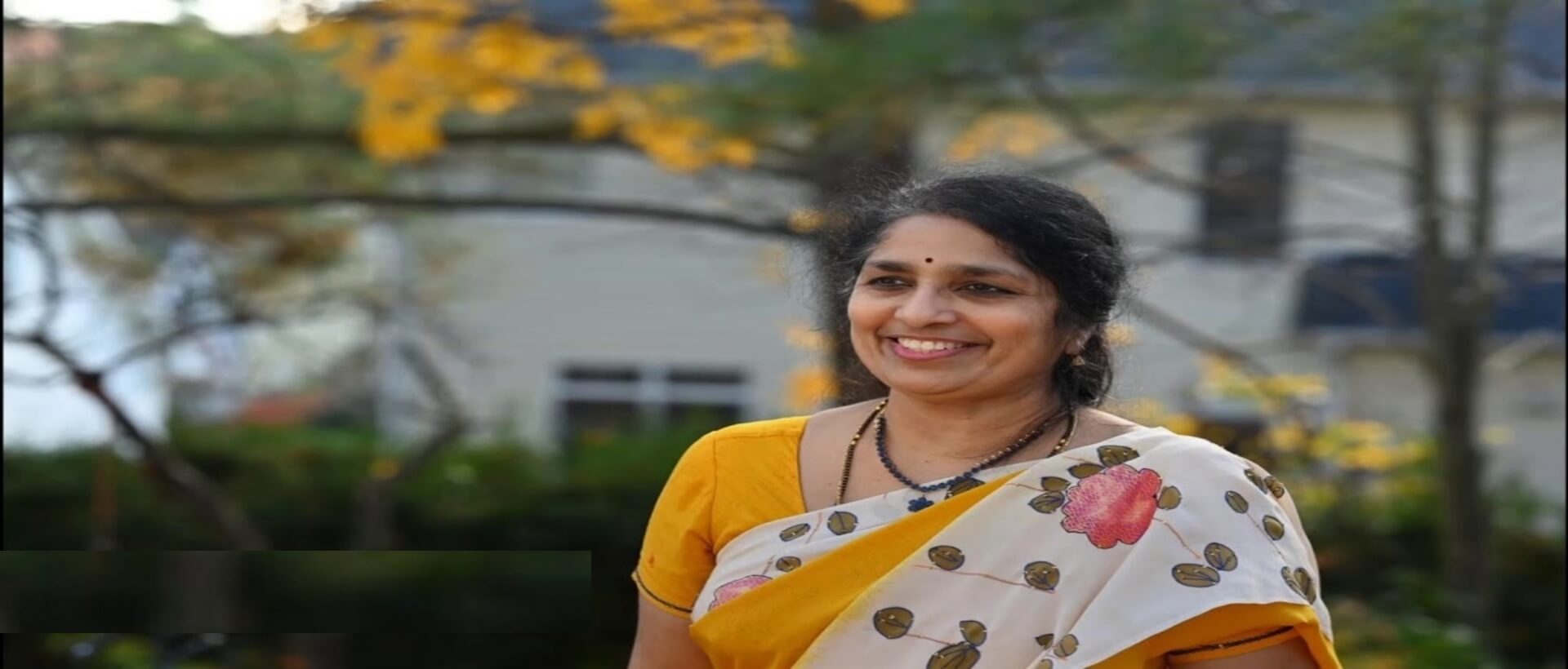 A woman in yellow and white sari smiling.